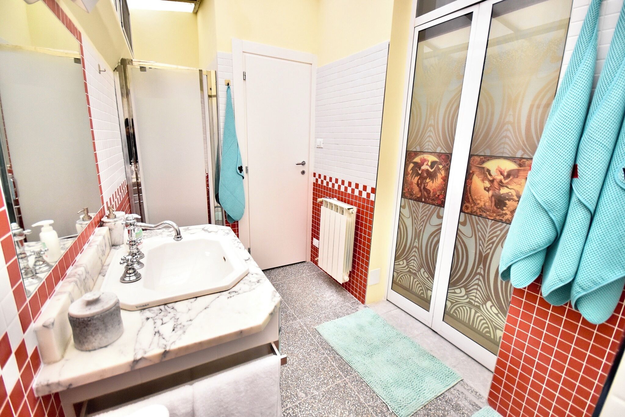 A bathroom with a marble sink, a towel rack, a shower with a glass door, and red and white tiled walls.