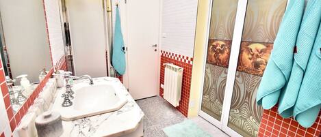 A bathroom with a marble sink, a towel rack, a shower with a glass door, and red and white tiled walls.