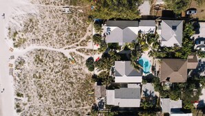 Ett flygbildsbild av en fastighet vid kusten med en swimmingpool, flera byggnader och ett sandstrandområde.