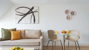 A modern living room with a sofa, a glass table with chairs, a painting, and wall decor. - Micklegate by Supercity Aparthotels (York)