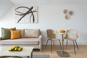 Een moderne woonkamer met een bank, een glazen tafel met stoelen, een schilderij en wanddecoratie.