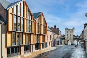 Une rue bordée d’immeubles modernes, d’une tour de pierre d’époque et d’une rue pavée.