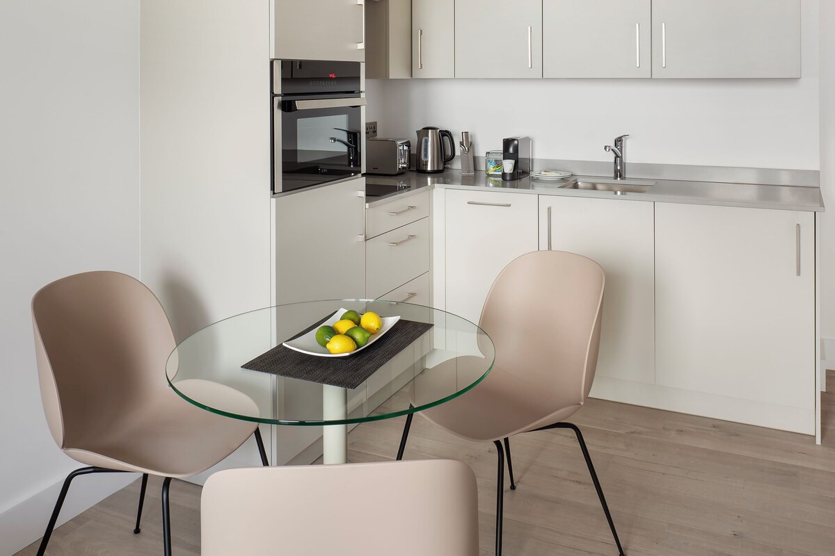 A modern kitchen with white cabinets, a glass dining table, and two chairs.