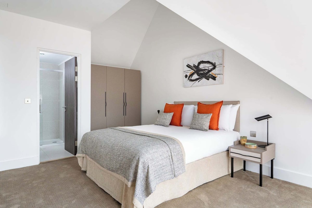 Un dormitorio con cama, mesita de noche, un cuadro y una puerta que da al baño.