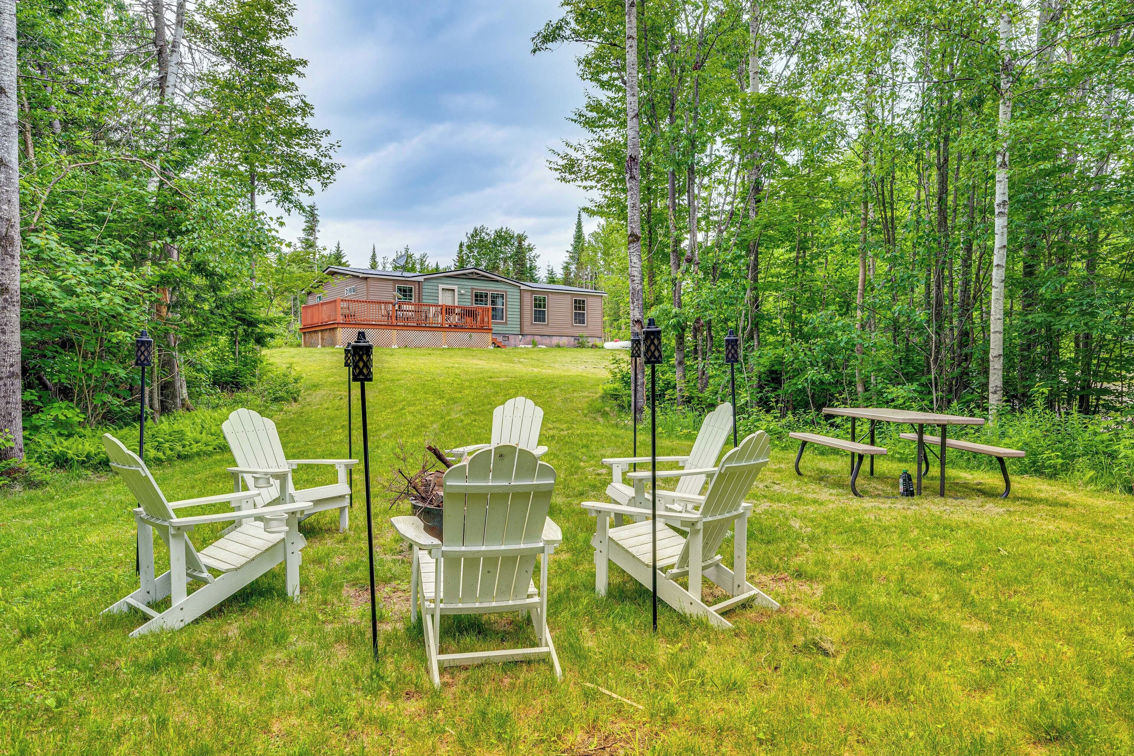 A house with a deck, surrounded by a grassy yard with Adirondack chairs and a picnic table.