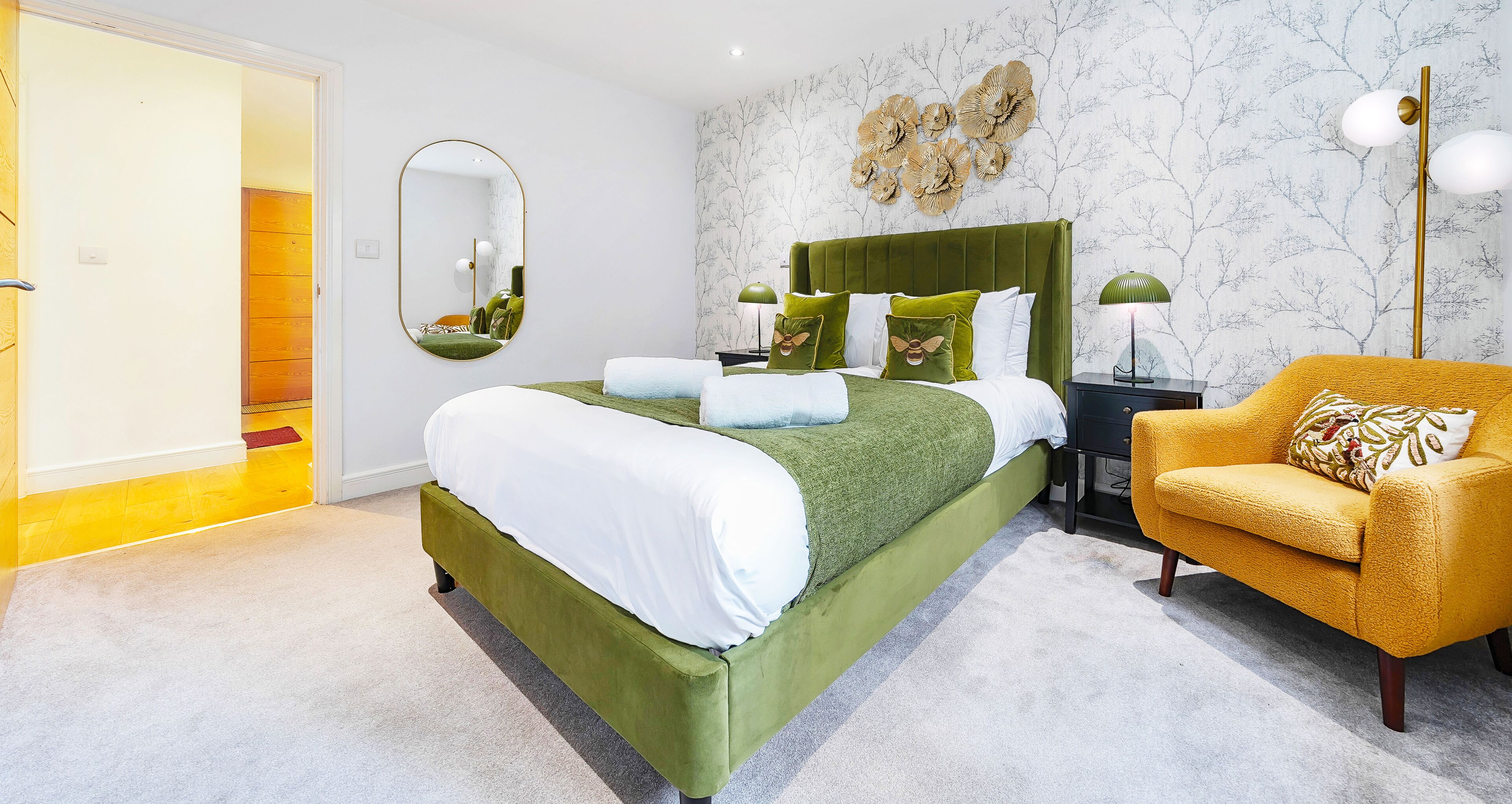 Ein modernes Schlafzimmer mit einem mit grünem Stoff bezogenen Bett, einem gelben Sessel und einem großen Spiegel.