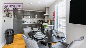 Un espace repas moderne avec une table noire dressée pour six personnes, des chaises grises à revêtement rembourré et un vase rempli de fleurs blanches.