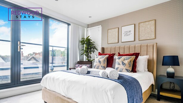 Une chambre moderne avec un grand lit, une plante en pot et des œuvres d’art accrochées au mur.