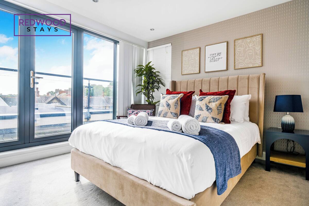 A modern bedroom with a large bed, a potted plant, and artwork on the wall.