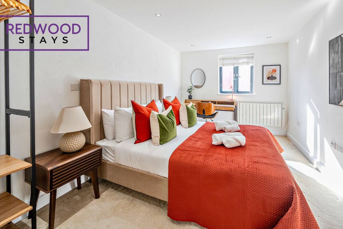 A hotel room with a bed, a nightstand, a lamp, a chair, a window, and a radiator.