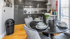 A modern dining area with a black table set for six, grey upholstered chairs, and a vase of white flowers. - High Street Apartments By REDWOOD STAYS (Camberley)