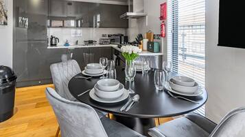 A modern dining area with a black table set for six, grey upholstered chairs, and a vase of white flowers.