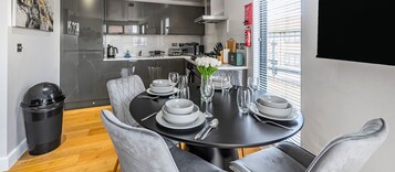 Uma sala de jantar moderna com uma mesa preta posta para seis pessoas, cadeiras estofadas cinzas e um vaso de flores brancas.