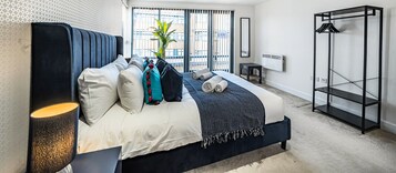 Un dormitorio moderno con una cama grande, una mesita de noche, un armario de pared y vistas a la ciudad a través de amplios ventanales.