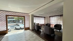 A spacious room with a wooden floor, two armchairs, a sofa, and a view of a parking lot through a glass door. - Al Salamh suites Family - أجنحة السلامة العائلية (Jeddah)