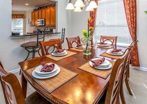 Uma sala de jantar com uma mesa de madeira posta para seis pessoas, rodeada por cadeiras.