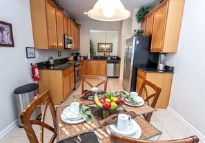 Uma cozinha compacta com armários de madeira, uma mesa de jantar posta para quatro pessoas e uma fruteira sobre a mesa.