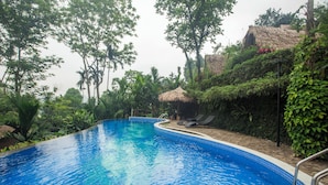 Una piscina de borde curvo, rodeada de abundante vegetación y una estructura con techo de paja.