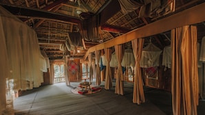 Una habitación tradicional con vigas de madera, techo de paja y cortinas colgantes.
