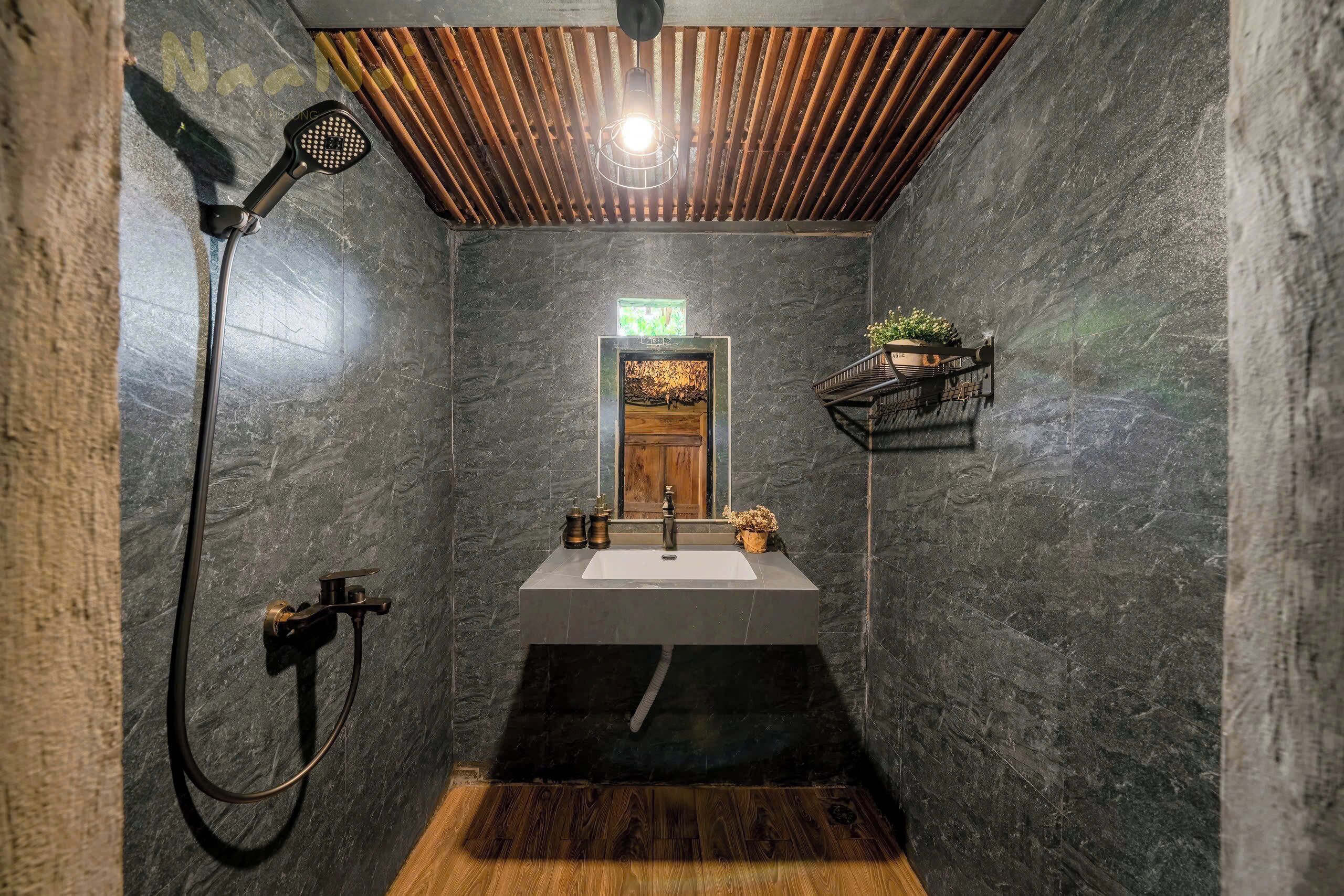 Een badkamer met een houten plafond, een wastafel met spiegel, een douche en een klein plankje met een plant.