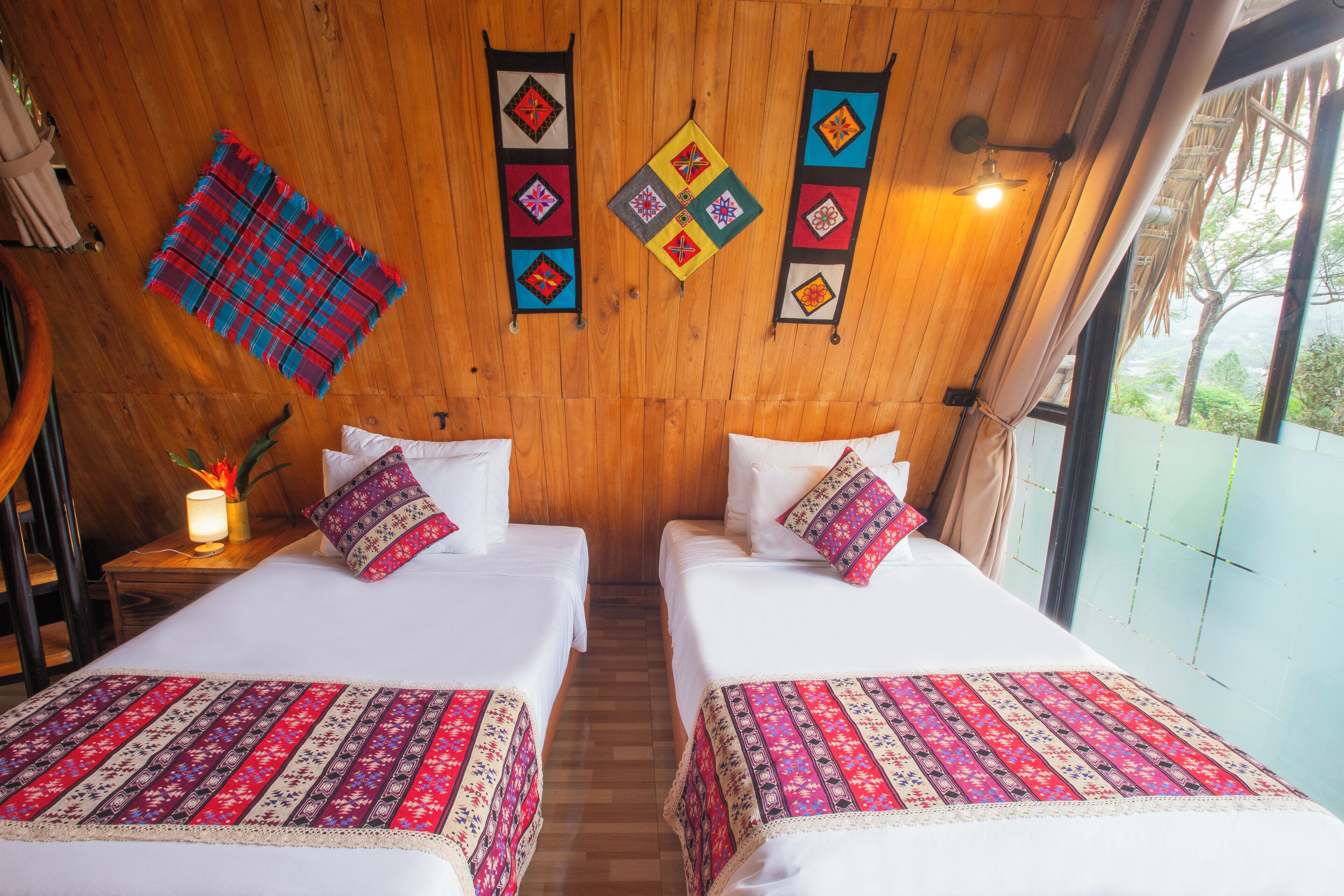 A room with two beds, wooden walls, and a view through a window.