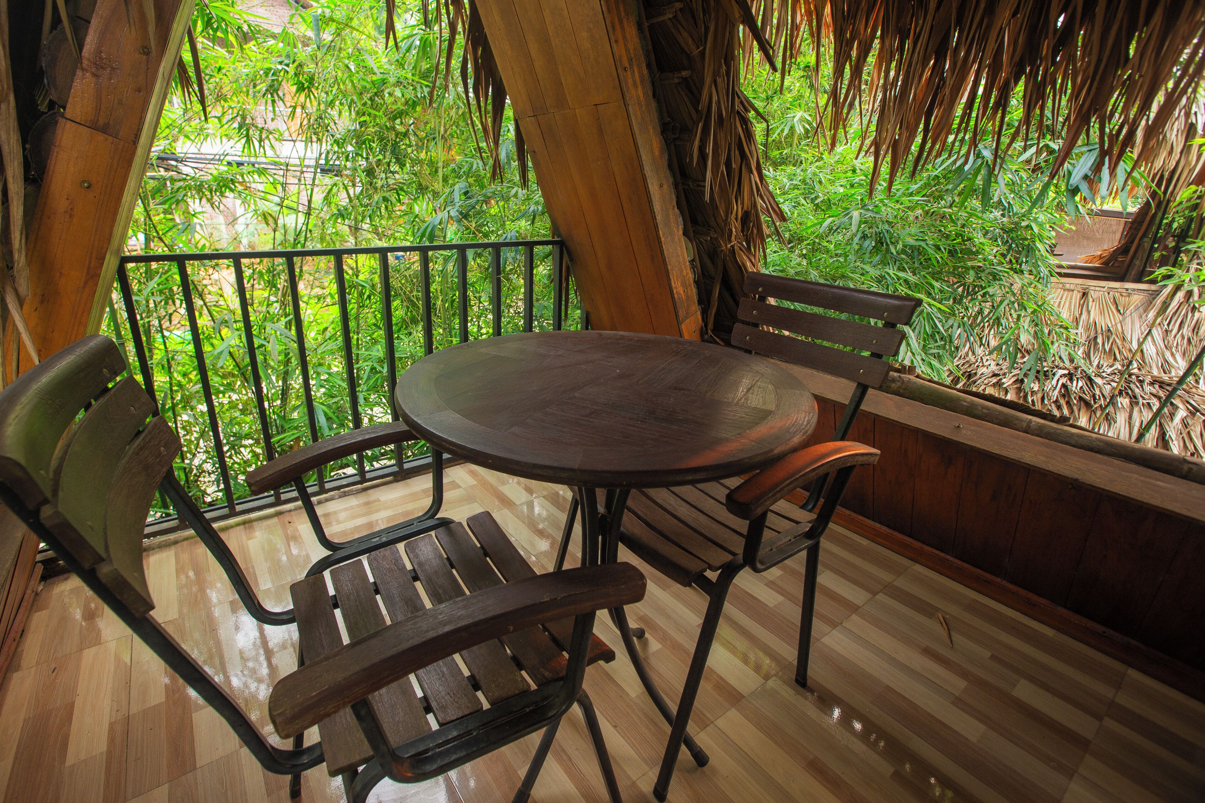 A wooden table and chairs on a balcony with a view of lush greenery.