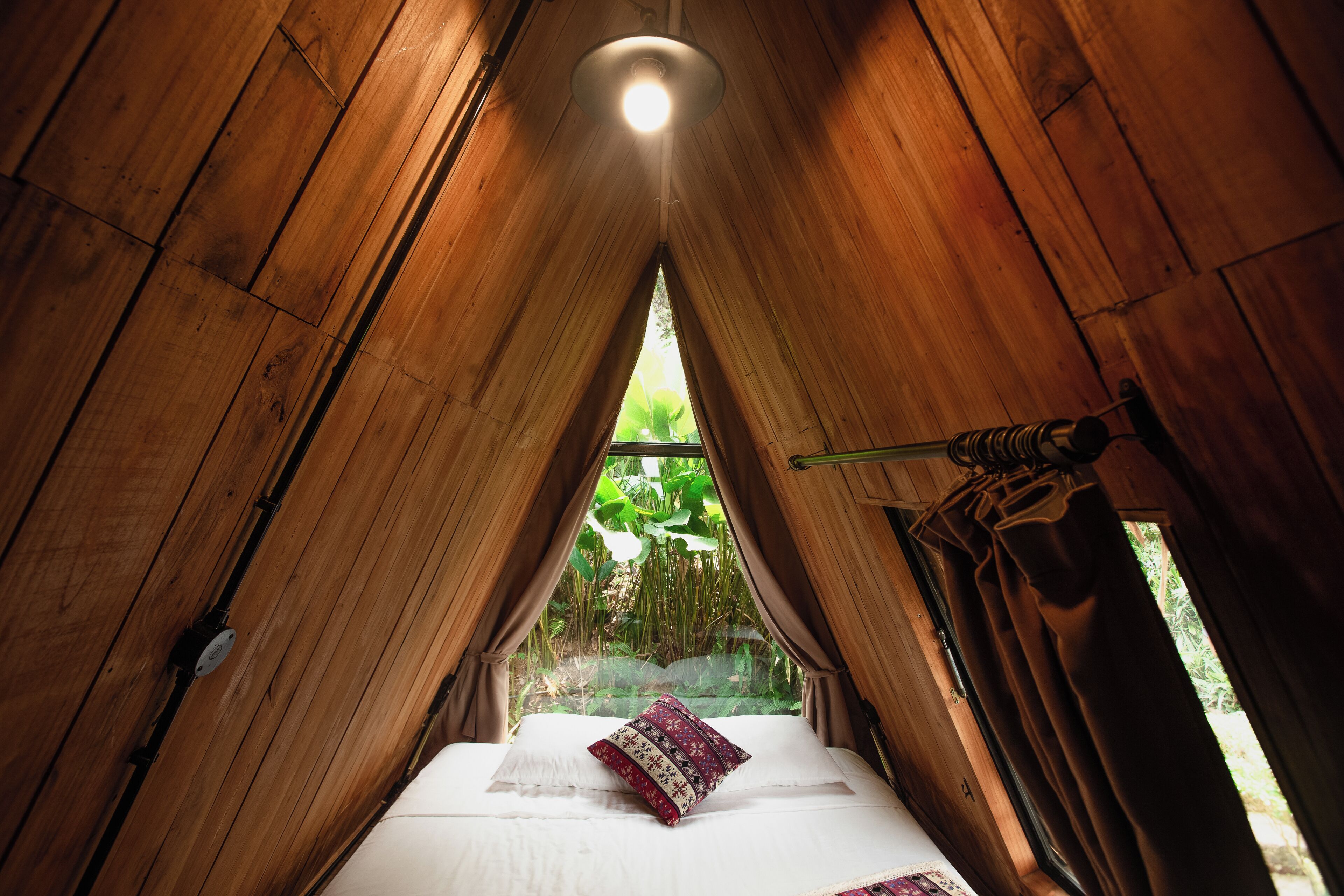 Een tentvormige kamer met een bed, gordijnen en een raam met uitzicht op groen.