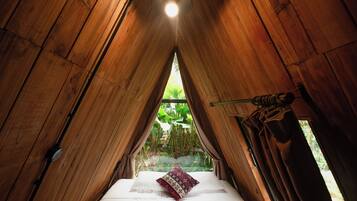 Een tentvormige kamer met een bed, gordijnen en een raam met uitzicht op groen.