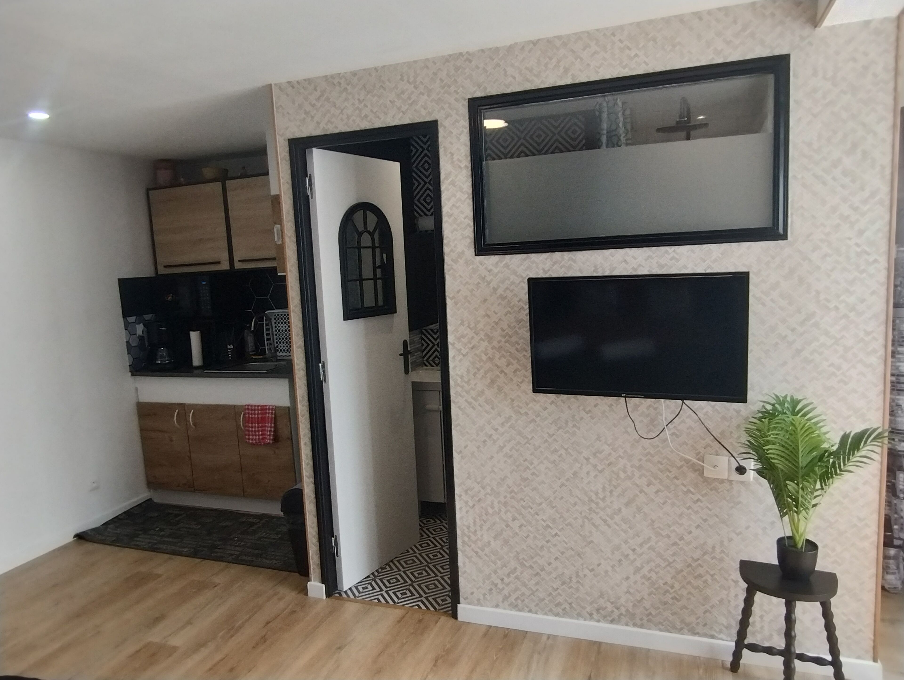 A modern kitchen with wooden cabinets, a black countertop, and a microwave. A door leads to a hallway with a patterned floor.