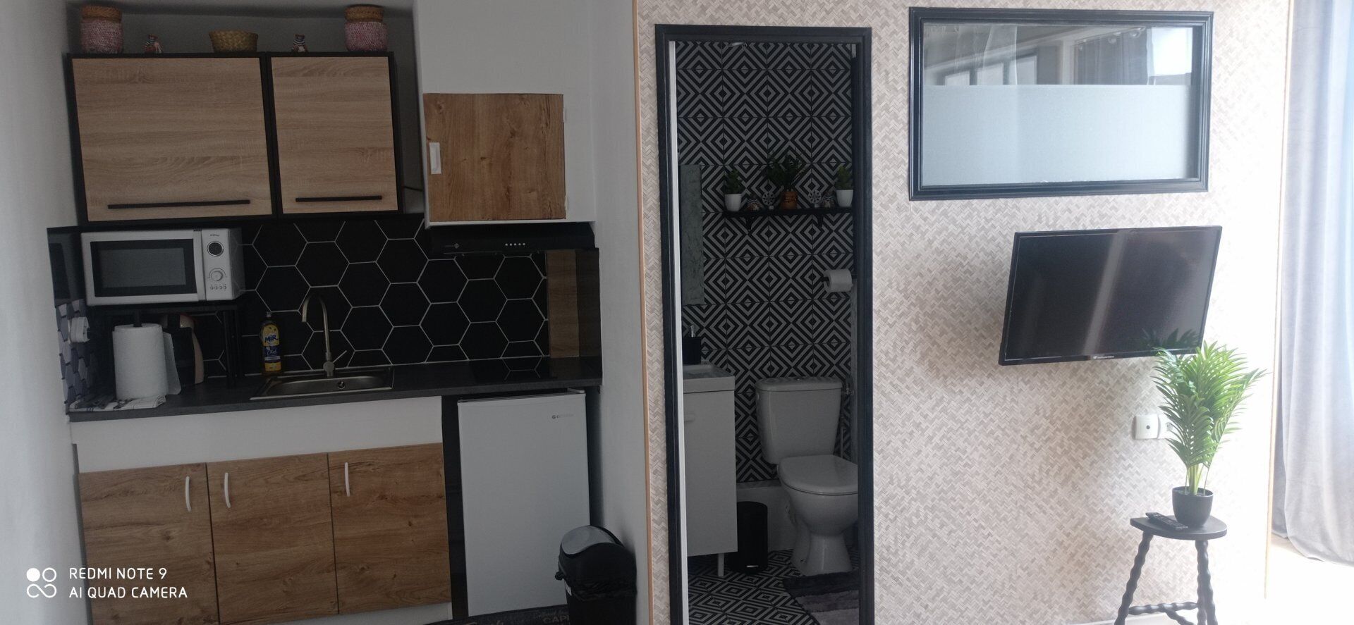 Eine kleine Küche mit Mikrowelle, einem Kühlschrank, Holzschränken und einer schwarzen Küchenzeile.