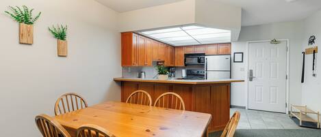 A compact kitchen with wooden cabinets, a central island, and a dining table with chairs.