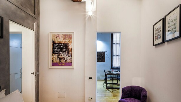 Una habitación de hotel con una cama, una silla morada, un cartel en la pared y vistas al comedor.