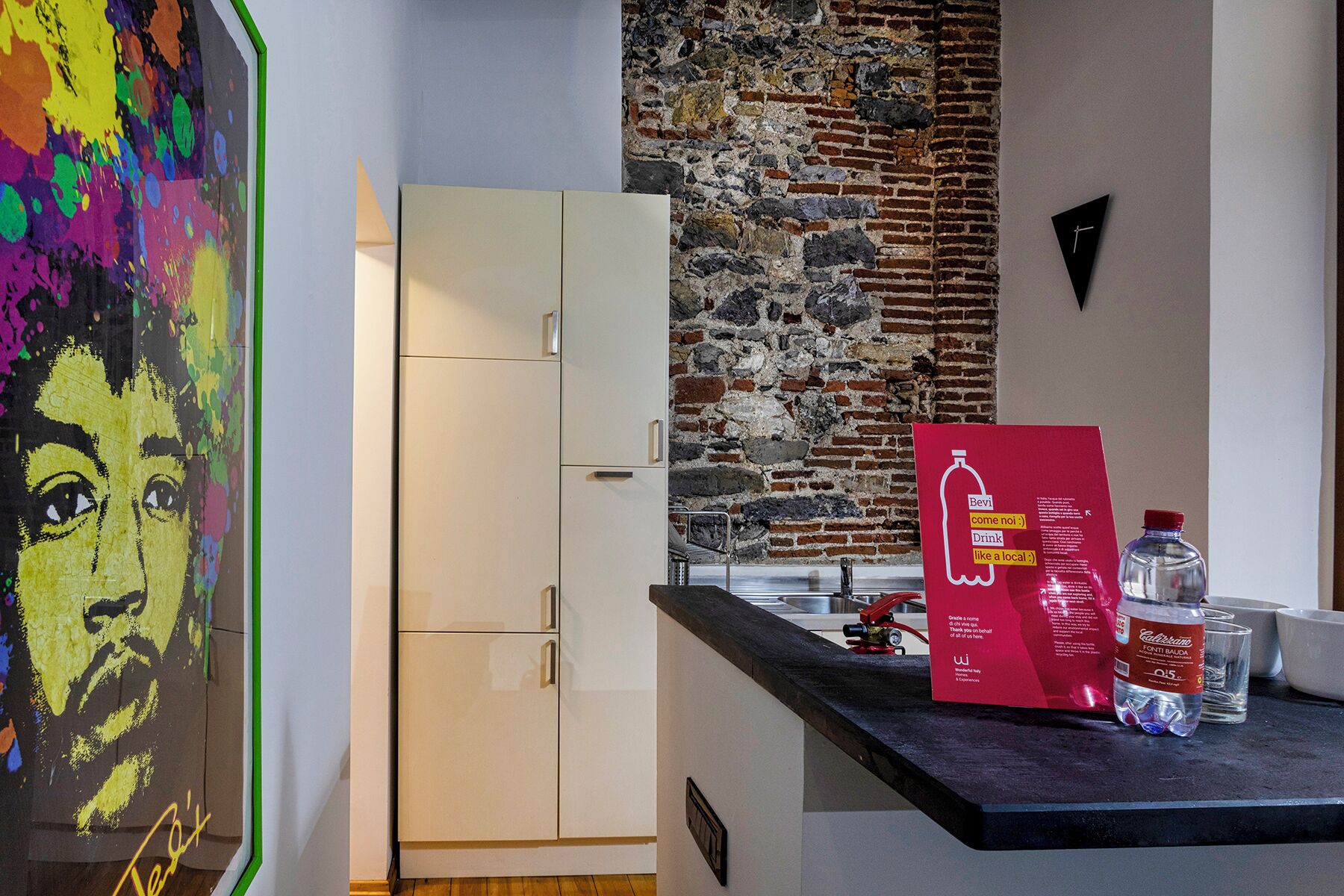 A kitchen with a white cabinet, a stone wall, a red sign, and a water bottle.