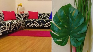 Sala de estar com sofá em formato de L, tapete vermelho e uma planta grande.