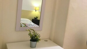 Um banheiro com pia branca, uma planta em vaso, um espelho e uma cama com travesseiro branco e uma luminária na mesa de cabeceira.