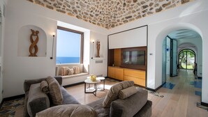 Ein modernes Wohnzimmer mit Stein Decke, einem großen Fernseher und Blick aufs Meer.