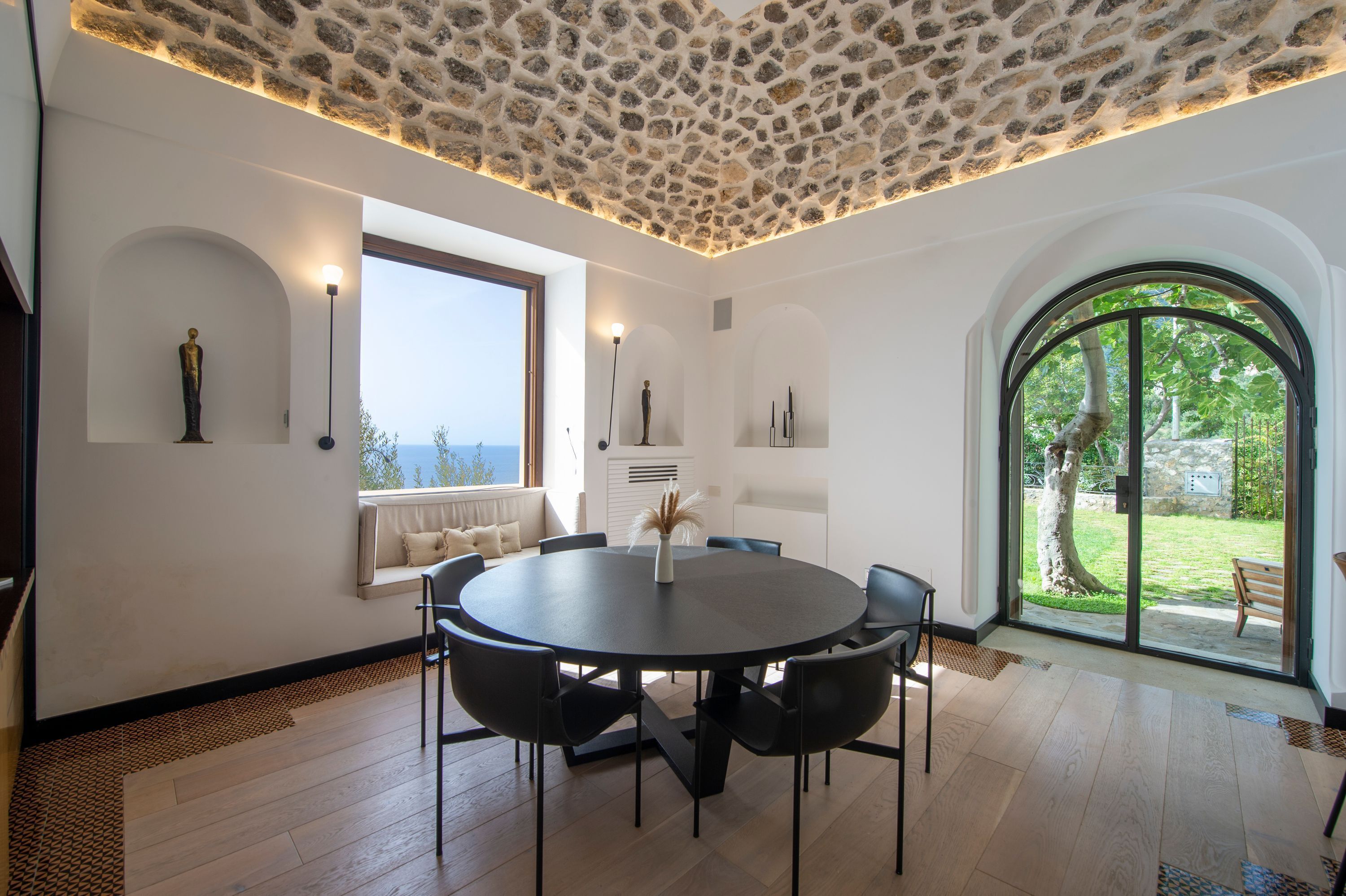 Un comedor moderno con una mesa redonda, sillas negras y techo de piedra.
