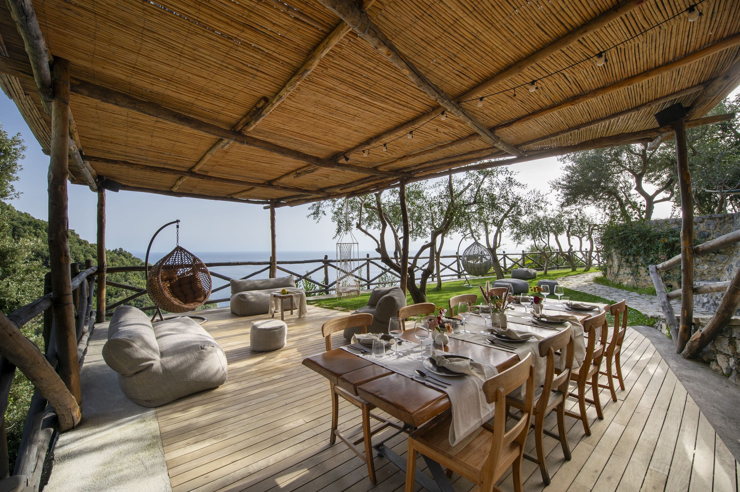 Un espace extérieur aménagé pour les repas, avec une terrasse en bois, un coin salon couvert et une vue sur la mer.