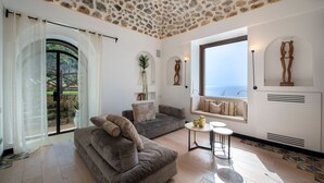 Ein modernes Wohnzimmer mit Steindecke, einem grauen Sofa, einem kleinen runden Tisch und Meerblick durch ein großes Fenster.