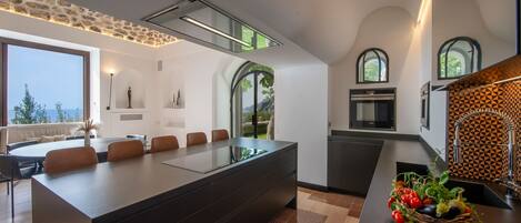 Una cocina moderna con una isla central, un comedor con una mesa grande y sillas, y vistas al exterior.