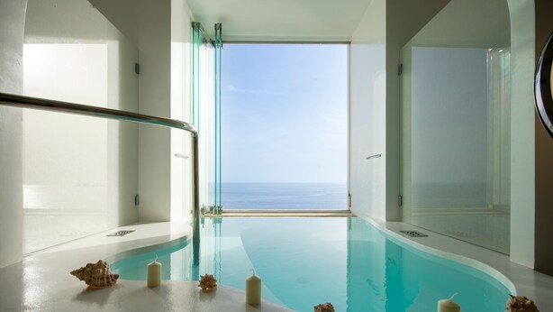 Ein Pool mit freiem Blick auf das Meer, umgeben von weißen Wänden und einer Glasumlaufung.