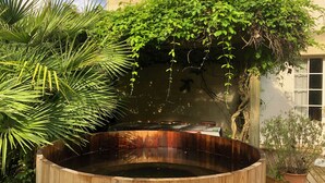 Un bain à remous en bois, entouré d’une végétation luxuriante et bordé d’un mur de pierres.