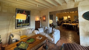 Un salon chaleureux avec une table basse en bois, un canapé et une cheminée. On aperçoit à l’arrière-plan un coin repas avec une table et des chaises.