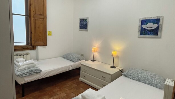 Une chambre avec deux lits simples, une armoire en bois, une table de chevet avec des lampes et un radiateur.