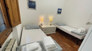 Une petite chambre propre, avec deux lits simples, une armoire en bois et deux lampes fixées au mur.