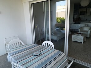 A balcony with a table and chairs, a sliding glass door, and a view of the interior including a kitchen and a dining area.