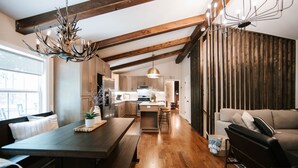 A spacious kitchen with wooden beams, a dining area with a bench, and a living room with a sofa. - Blue Ridge Haven is packed with luxury and family fun including a Hot Tub, Creekside Fire Pit, Game Room, Private Yard with Playset, and Back Deck with Grill. Your stay is owned and managed by a four time AirBnB Superhost. (Blue Ridge)
