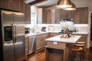 A modern kitchen with stainless steel appliances, wooden cabinets, and a central island with stools. - Blue Ridge Haven is packed with luxury and family fun including a Hot Tub, Creekside Fire Pit, Game Room, Private Yard with Playset, and Back Deck with Grill. Your stay is owned and managed by a four time AirBnB Superhost. (Blue Ridge)