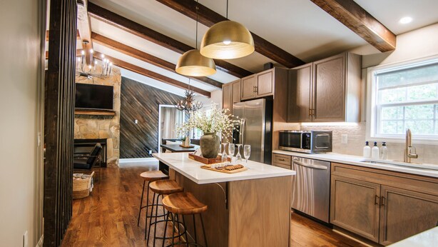 A modern kitchen with a large island, wooden bar stools, and a stone fireplace. - Blue Ridge Haven is packed with luxury and family fun including a Hot Tub, Creekside Fire Pit, Game Room, Private Yard with Playset, and Back Deck with Grill. Your stay is owned and managed by a four time AirBnB Superhost. (Blue Ridge)