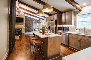A modern kitchen with a large island, wooden bar stools, and a stone fireplace. - Blue Ridge Haven is packed with luxury and family fun including a Hot Tub, Creekside Fire Pit, Game Room, Private Yard with Playset, and Back Deck with Grill. Your stay is owned and managed by a four time AirBnB Superhost. (Blue Ridge)